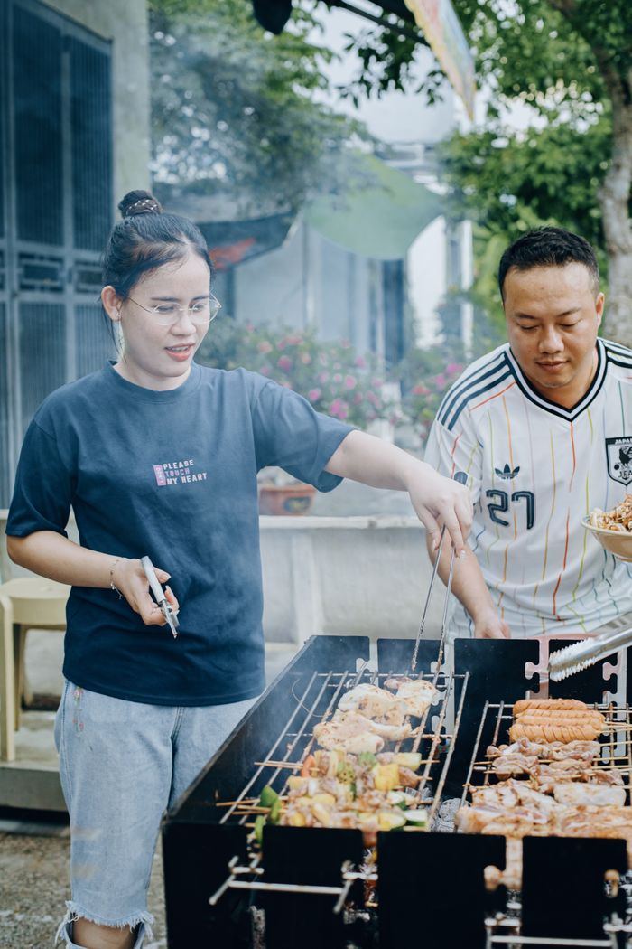 Two adults enjoy grilling assorted meats outdoors, creating a lively social atmosphere.